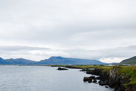 Tranquil seascape featuring cliffs, water, and mountain views under a cloudy sky