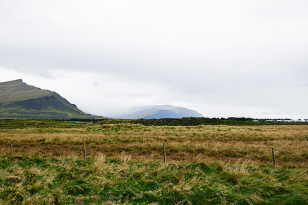 Expansive Icelandic grasslands with distant mountains, cloudy skies, and rustic fencingの写真素材