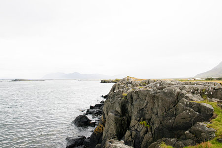 A rugged coastal scene featuring rocks, water, and Iceland's distant mountain range.