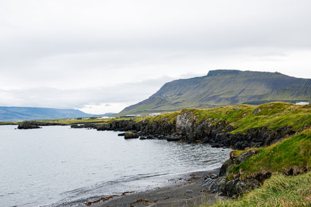 Tranquil coastal scene in Iceland featuring rocky shores, mountains, and peaceful watersの写真素材