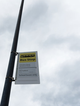 Bus Stop sign on a metal pole under cloudy sky in Manchester, guiding school buses.の写真素材