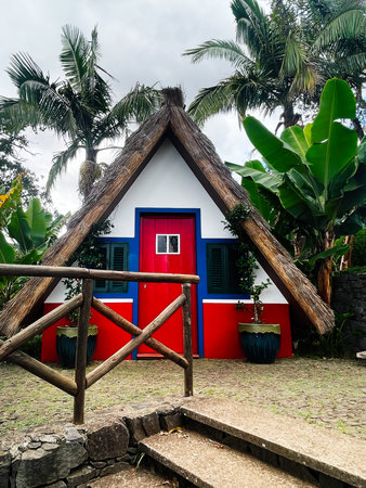 Bright thatched cottage in Madeira Portugal with a red door, blue trim and lush tropical plants.の写真素材