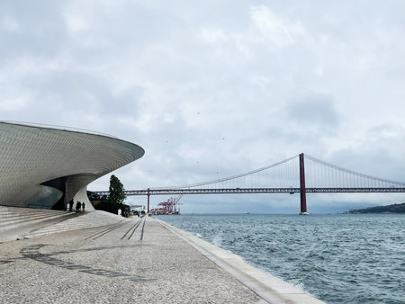 Contemporary waterfront scene in Lisbon showing the MAAT museum, riverfront walkway, and the red bridge across the Tagus.の写真素材