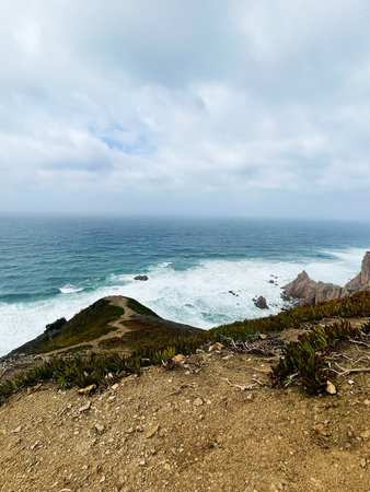 Rocky cliff trail by the sea under cloudy skies, showcasing coastal scenery.の写真素材