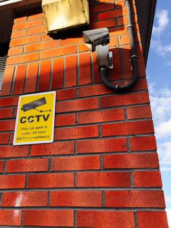 Yellow CCTV sign beside a security camera on a brick building in Manchester, UK.の写真素材