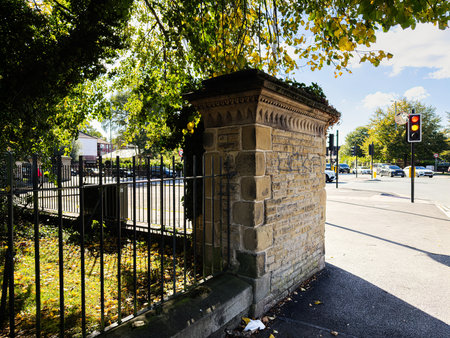 Stone pillar and iron fence frame a Manchester city street, with traffic, trees and sunlight.の写真素材