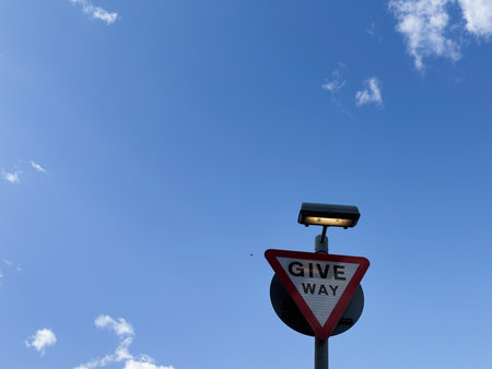 Triangular give way sign with street lamp against a bright blue sky in Manchester UK.の写真素材