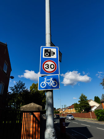 Blue sky over a Manchester road features a speed sign and bicycle sign on a metal pole.の写真素材