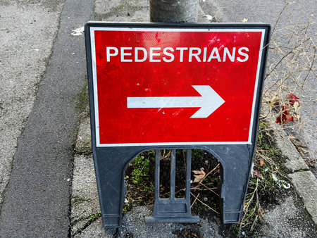 Red pedestrian sign with right arrow on a Manchester street, urban safety and visibility in a city setting.の写真素材