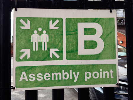Green assembly point sign in Manchester with people icons under arrows indicating a meeting area.の写真素材