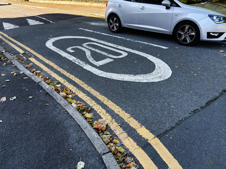 A white hatchback parked on a Manchester street beside a large 20 mph marking.