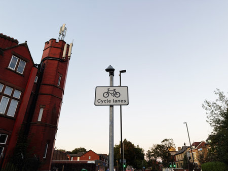 A cycling sign stands beside a red brick building on a Manchester street at dusk.の写真素材