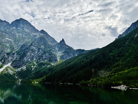 A serene alpine lake mirrors dramatic mountains and dense forest in Zakopane, Poland.の写真素材