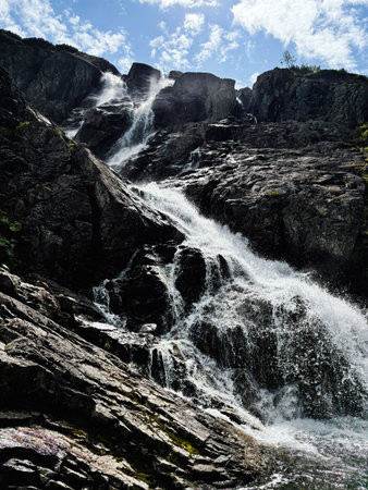 A powerful waterfall flows over dark rocks under a bright sky, capturing motion and natural drama.の写真素材