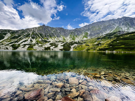 A serene alpine lake in Zakopane Poland surrounded by rocky slopes and green meadows.の写真素材