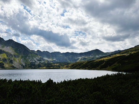 A tranquil alpine lake with dramatic clouds over rugged peaks in Zakopane Poland and green meadows.の写真素材