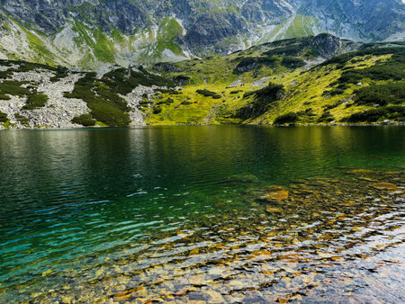 Crystal clear lake mirrors green hills and rocky slopes in Zakopane, surrounded by dramatic...