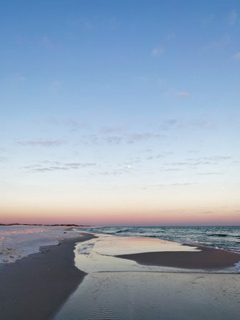 Serene Florida coast at sunset with calm water, soft pastel sky and wide sandy shoreline.の写真素材