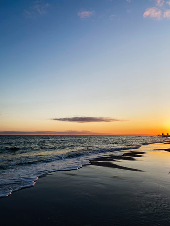 Golden sunset over a tranquil Florida beach with gentle waves and a distant city skyline.の写真素材