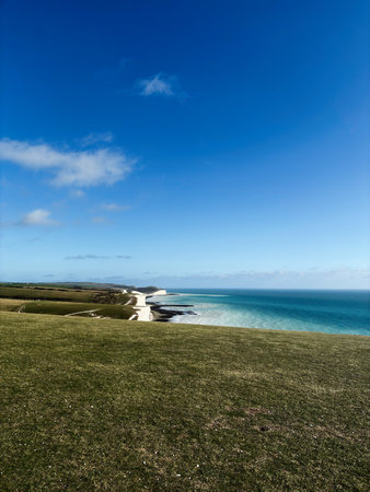 Vast coastal landscape at Seven Sisters Cliffs, blue sky, emerald fields, and turquoise sea.の写真素材