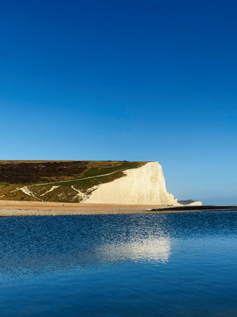 White chalk cliffs rise above blue water at Seven Sisters in East Sussex, a striking coastal landscape.の写真素材