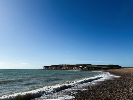Bright sky over pebble beach and white cliffs at Seven Sisters with calm ocean.