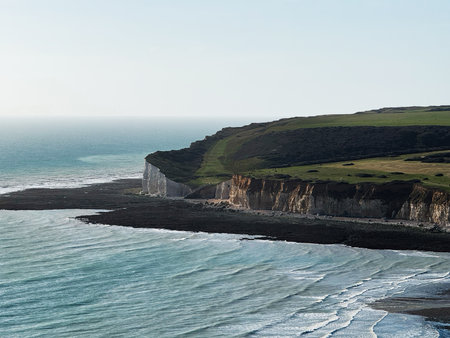 Dramatic coastal landscape with white cliffs, green fields, and blue sea along the shore.