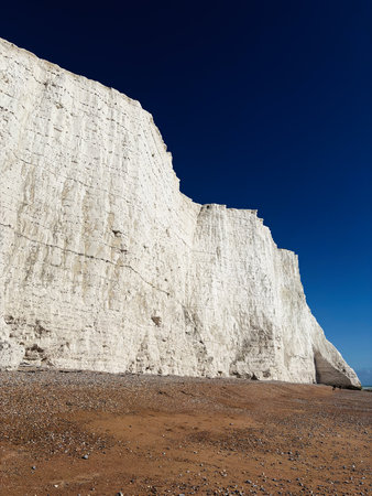 Scenic chalk cliffs rise above a pebbled beach under a deep blue sky, highlighting dramatic coastal...