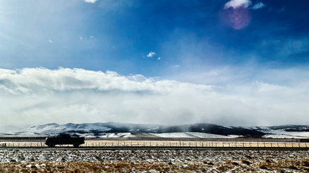 A lone pickup travels a snow covered highway in Utah, mountains in the distance and clear sky.の写真素材