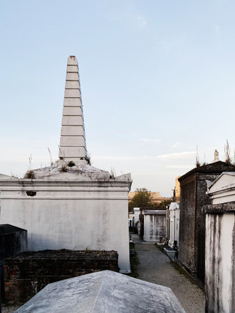 A lone obelisk monument rises in a historic New Orleans cemetery, calm and weathered.