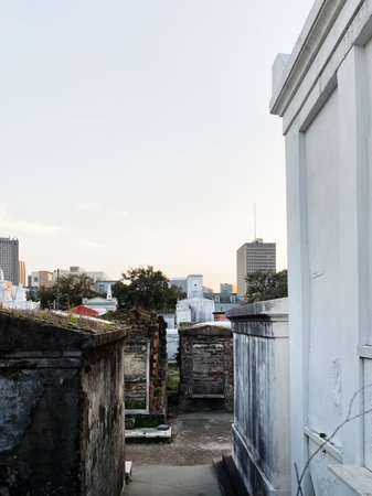 Weathered tombs amid an old cemetery in New Orleans with distant city skyline at dusk.