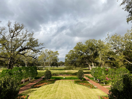 Serene garden scene in Vacherie, St. James Parish featuring trimmed hedges, open lawn, and winding brick walkways under a moody sky.の写真素材