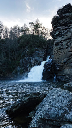 A dramatic Linville Falls waterfall pours between rugged rocks, with trees lining the canyon and a dark river below.の写真素材