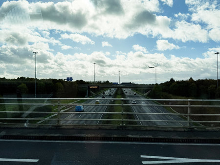 Dublin, Ireland - October 21, 2025: Vehicles move along a multi lane highway in Ireland beneath a blue sky and scattered clouds, with an overpass and green scenery.のeditorial素材