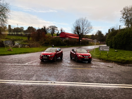 Longford, Ireland - October 21, 2025: Two red Nissan Qashqai cars at a crossroads in a rain soaked Irish countryside near a village.のeditorial素材
