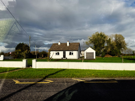 Edgeworthstown, Ireland - October 21, 2025: Peaceful Irish countryside scene featuring a white house, detached garage, green lawn, and dramatic sky.のeditorial素材
