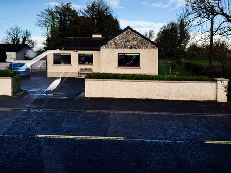 Longford, Ireland - October 21, 2025: Calm residential scene in Ireland featuring a single-story house with a stone facade, front garden, and bright sky.のeditorial素材