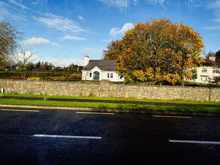 Longford, Ireland - October 21, 2025: White cottage in Ireland beside a stone wall and vibrant autumn tree under blue skies.のeditorial素材