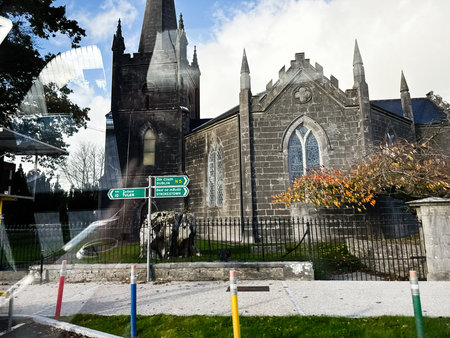 Curraghmore, Ireland - October 21, 2025: Stone church in Ireland with Gothic arches, a wrought fence, and road signs in autumn light.のeditorial素材