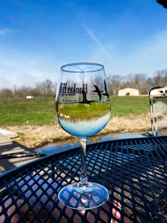 Indiana, USA - April 12, 2025: A glass of Honker Hill Winery white wine on a metal patio table outdoors in Indiana, USA, under a bright blue sky.のeditorial素材