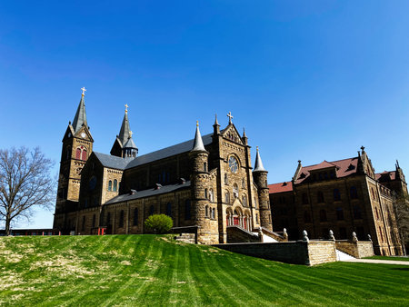 St Meinrad, Indiana, USA - April 12, 2025: Grand stone Saint Meinrad Archabbey church with towers and steps on manicured grounds in Indiana under a bright blue sky.のeditorial素材