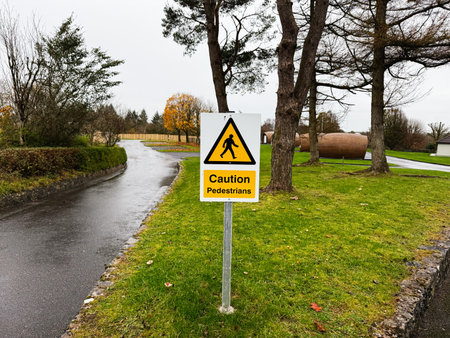 Knock, Ireland - October 22, 2025: Yellow caution sign for pedestrians beside a tree lined park road in Knock Ireland.のeditorial素材
