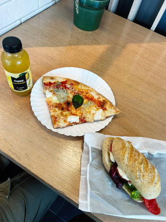 Tarnow, Poland - October 25, 2025: Casual meal setup with cheese pizza, sandwich, and orange juice on a wooden table.のeditorial素材
