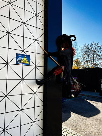 Kyiv, Ukraine - October 25, 2025: A silhouetted witch climbs a wall with a broom beside a modern geometric exterior on a sunny day.のeditorial素材