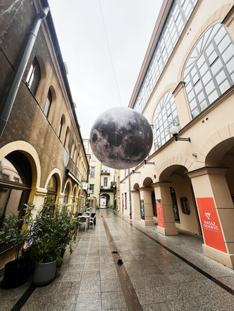 Tarnow, Poland - October 25, 2025: A wide street scene shows a large suspended moon sculpture between historic arches and cafe seating in Tarnow, Poland.のeditorial素材