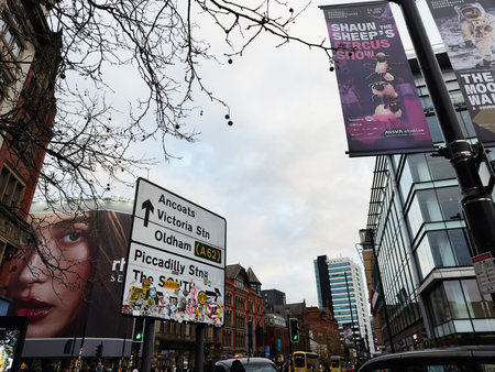 Manchester, UK - November 16, 2025: Busy Manchester street with a large signpost directing to Ancoats, Victoria Station, Oldham and Piccadilly Station amid modern buildings and banners.のeditorial素材