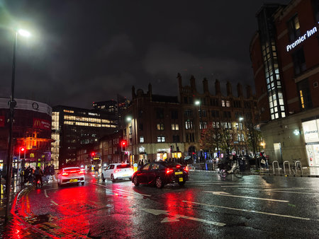 Manchester, UK - November 14, 2025: Nighttime urban scene in Manchester featuring wet streets, moving cars, pedestrians, and glowing storefronts.のeditorial素材