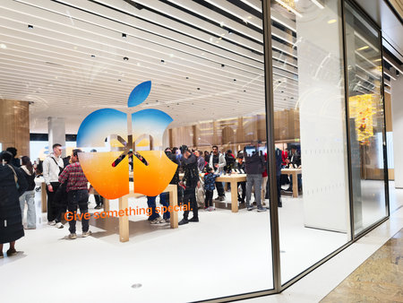 Stretford, UK - November 15, 2025: Busy Apple store in Manchester with customers exploring devices at tables, bright interior, and a large store logo on glass.のeditorial素材