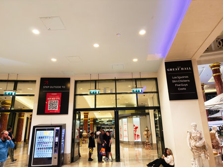 Stretford, UK - November 15, 2025: Inside a Manchester mall, people gather near vending machines and signboards under blue lighting.のeditorial素材