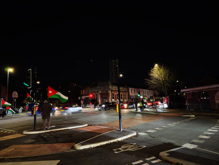 Manchester, UK - November 19, 2025: Nighttime Manchester street with Palestine protest flags, cars, pedestrians and city lights at a busy intersection.のeditorial素材